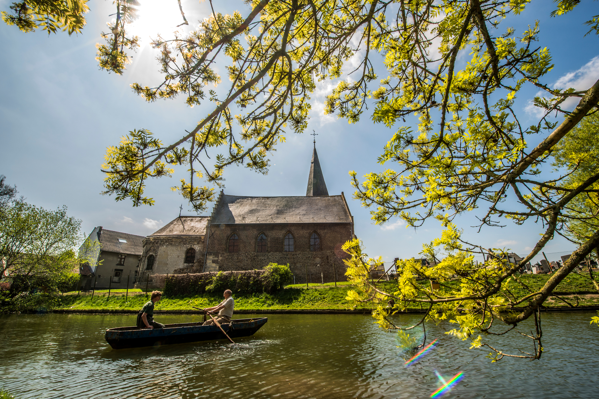 Zonnige foto van de Salviuskerk in Limbricht met een bootje die aan het roeien is in de vijver.